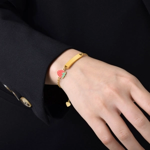 Macro shot of gold strawberry charm bracelet with a rectangular blank metal plate on wrist