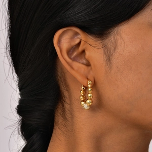 Gros plan de boucles d'oreilles créoles dorées avec perles et sphère sertie de zircons