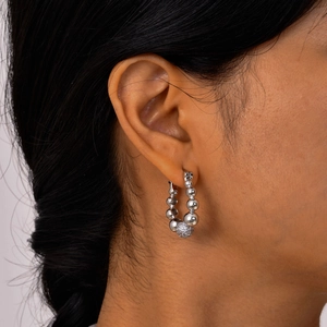 Détail d'une boucle d'oreille créole argentée perlée avec zircone sur l'oreille