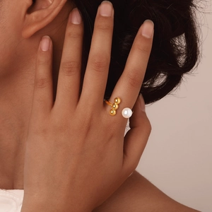 Gouden open ring met drie metalen kralen en een witte parel aan de vinger