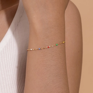 Close-up of golden beaded bracelet on wrist featuring vibrant colorful enamel charms