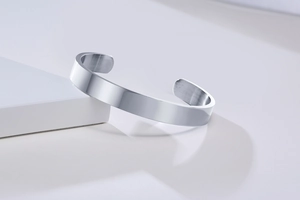 Polished stainless steel open cuff bracelet on a white geometric display stand