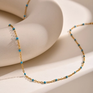 Minimalist gold stainless steel necklace with small blue beads on ceramic display
