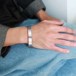 Polished stainless steel open cuff bracelet worn by hand over denim fabric detail
