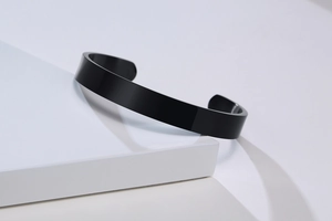 Minimalist black stainless steel C-shaped cuff bracelet on a white geometric display