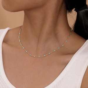 Golden stainless steel necklace with light blue beads on a female model neck