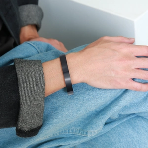 Detail of matte black stainless steel cuff bracelet worn on wrist against blue denim