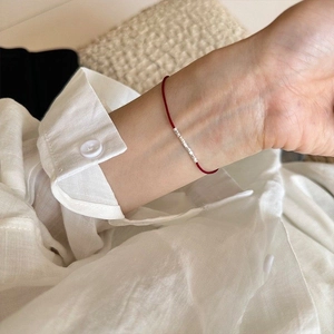 Detailansicht eines minimalistischen roten Stoffarmbands mit silbernen Perlen am Handgelenk