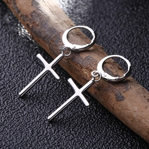 Détail des boucles d'oreilles créoles croix en argent poli suspendues à une branche de bois