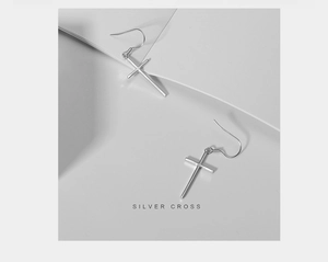Gros plan sur des boucles d'oreilles croix en argent poli sur un fond de papier géométrique