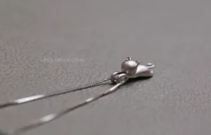 Macro di una collana con ciondolo a gatto in argento opaco su fondo grigio ruvido