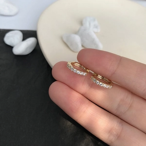 Close-up of gold huggie earrings with white crystals held to show compact size