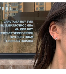 Detalle de pendientes de plata con mariposa y cruz con circonitas en una modelo femenina
