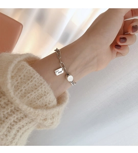 Detail eines silbernen S925 Good Luck Armbands am Handgelenk mit Strickärmel-Hintergrund