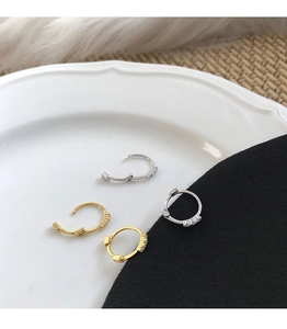 Detalle de mini pendientes de aro plateados y dorados con tres circonitas en una bandeja