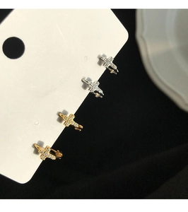 Detalle de pendientes en forma de cruz con brillantes blancos en acabados oro y plata