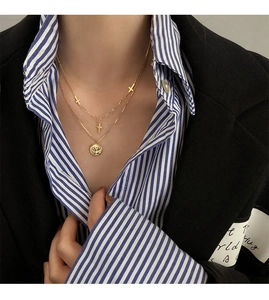 Primer plano de un collar dorado de doble capa con pequeñas cruces y colgante de moneda
