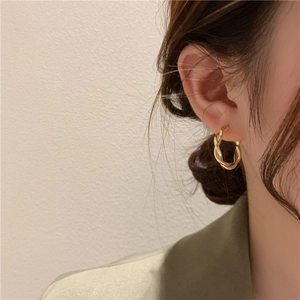 Eleganti orecchini a cerchio a corda intrecciata d'oro indossati da una modella su sfondo crema