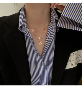 Detalle de collar dorado de doble capa con cruces y colgante de moneda redondo