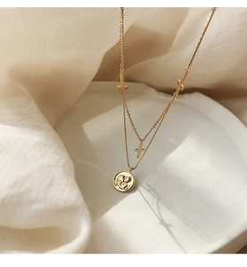 Detalle de collar de doble capa chapado en oro con colgante de moneda y pequeñas cruces
