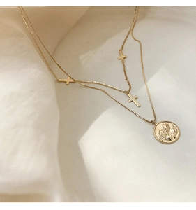 Detalle de collar dorado de doble capa con colgante de moneda y pequeñas cruces