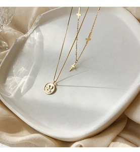 Detalle de collar dorado de doble capa con colgante de ángel y pequeñas cruces en bandeja