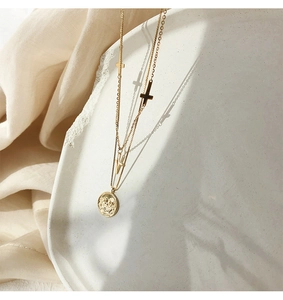 Detalle de collar doble dorado con colgante de moneda y pequeños amuletos de cruz