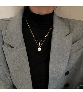 Primer plano de un collar dorado de doble capa con colgantes de cruz y una moneda redonda