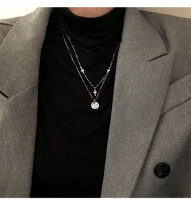 Detalle de collar doble plateado con cruz y colgante en relieve sobre traje gris