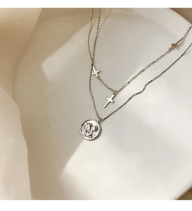 Detalle de collar de plata de doble capa con dijes de cruz y colgante de moneda redonda