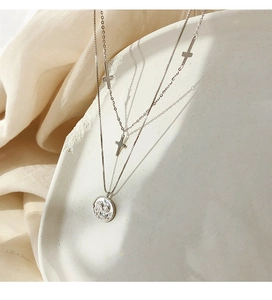 Detalle de collar de plata 925 de dos capas con colgante de moneda y dijes de cruz