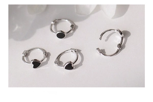 Dettaglio macro di orecchini minimalisti in argento a cuore e tondi con smalto nero