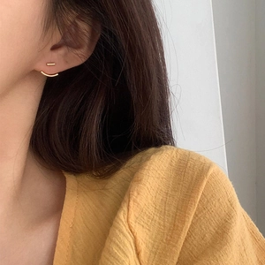 Orecchini minimalisti in oro a barra e curva indossati per un look chic e moderno