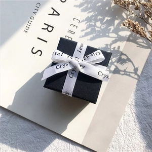 Elegant black square jewelry gift box with white ribbon bow and textured cross pattern