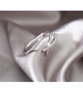 Detalle de anillo cruzado plateado con circonitas brillantes sobre tela de seda