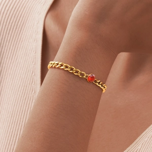 Dettaglio di un bracciale a catena cubana dorato con zircone rosso ovale indossato al polso