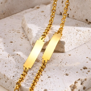 Polished gold stainless steel curved bar pearl chain bracelet on a travertine stone base