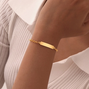 Gedetailleerd beeld van een gouden roestvrijstalen bar-armband met parelketting om pols