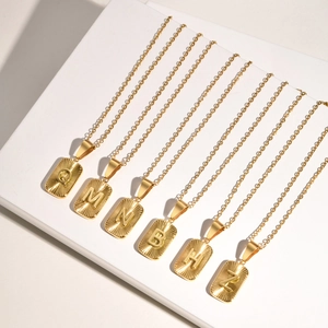 Gold stainless steel initial pendant necklaces with sunburst texture on a white stand