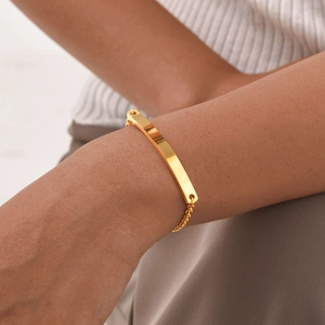 Detail of a gold stainless steel pearl chain bracelet with a curved metal nameplate on wrist