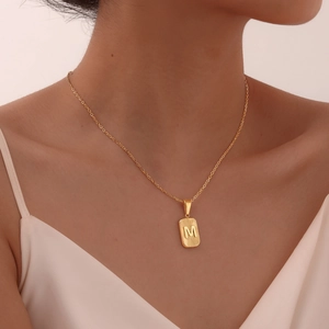 Detail of gold rectangular M pendant with sunburst texture on a thin chain link