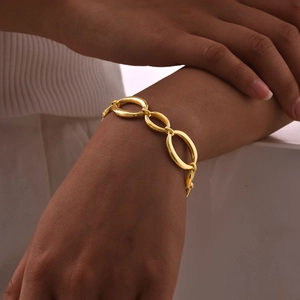 Gros plan d'un bracelet à grosses mailles ovales dorées porté par un mannequin femme