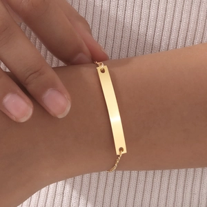 Detailed close-up of a minimalist gold bar bracelet worn by a model on a soft background