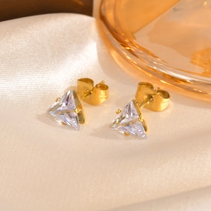 Detail of golden triangle zircon stud earrings on elegant silk background with soft lighting
