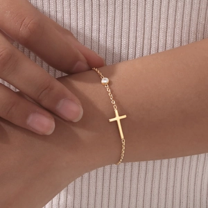Nahaufnahme eines goldenen Kreuzarmbands mit Zirkon, am Handgelenk getragen
