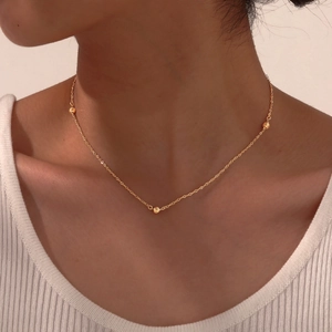 Détail du collier à billes dorées sur le cou avec trois perles métalliques facettées