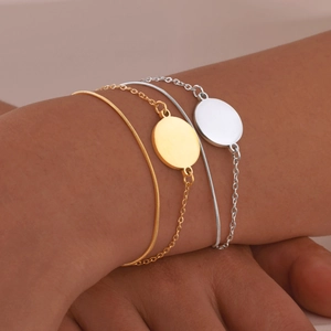 Minimalist gold and silver layered chain bracelets with polished blank round charms on wrist