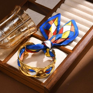Nahaufnahme des goldenen Hammerschlag-Armreifs mit geometrischem Seidenschal-Detail
