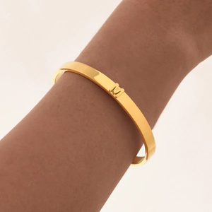 Primer plano de un brazalete dorado pulido con la letra M en 3D en la muñeca