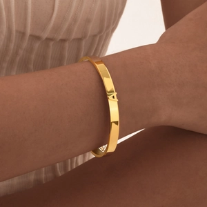 Primer plano de un brazalete de acero pulido dorado con detalle de letra A en 3D